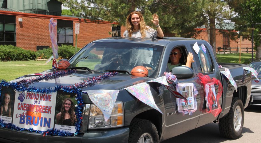 Jana Van Gytenbeek waves from the bed of a truck bearing lots of memorabilia, including what appear to be photos of her as a young child and, in the back, posters showing her as a girls basketball player and prom queen.